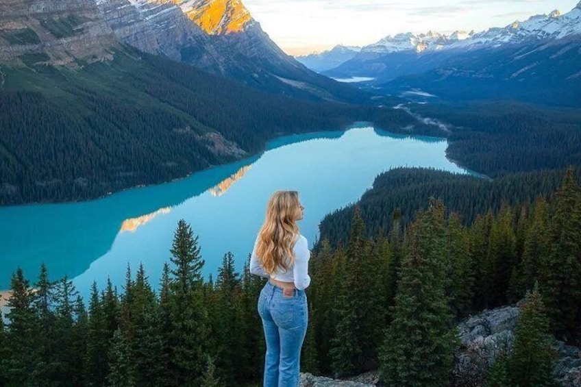Una persona de pie en una montaña, con vista a un lago turquesa rodeado de bosques densos y montañas. 3