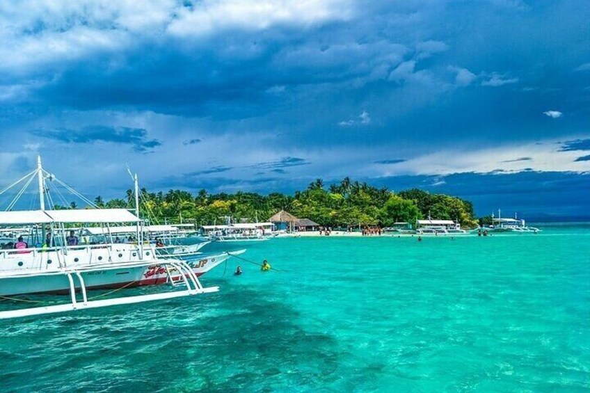 A clear turquoise sea with a boat docked near a small island with buildings and palm trees. 3
