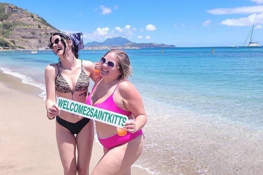 Two people on a beach holding a welcome sign. 3