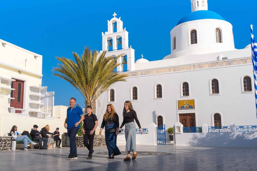 A white building with blue domes and a bell tower, palm trees, and people walking. 4