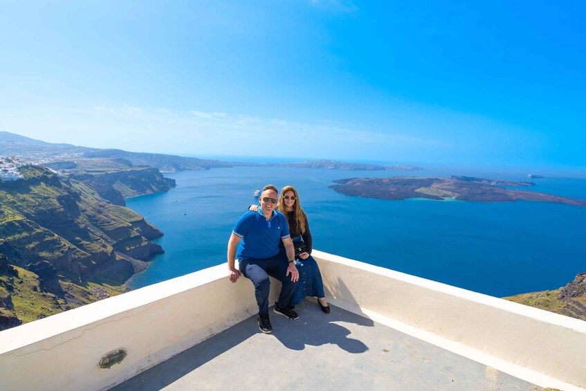 A couple sitting on a concrete ledge overlooking a coastal landscape with cliffs and a body of water. 3