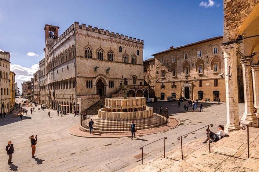 Une place historique, dominée par un bâtiment remarquable, caractérisé par ses fenêtres en arc et une fontaine centrale. 1