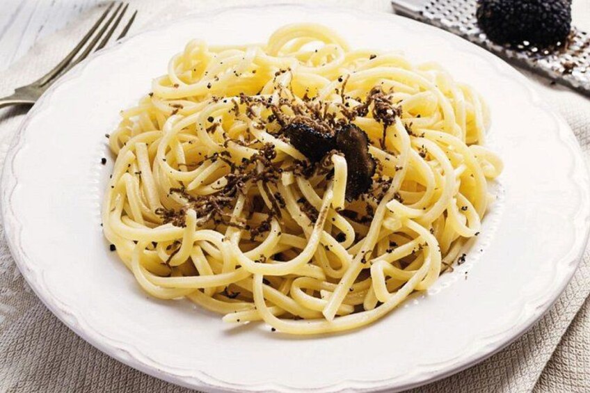 A plate of spaghetti with a black topping, possibly truffle, on a white plate. 2