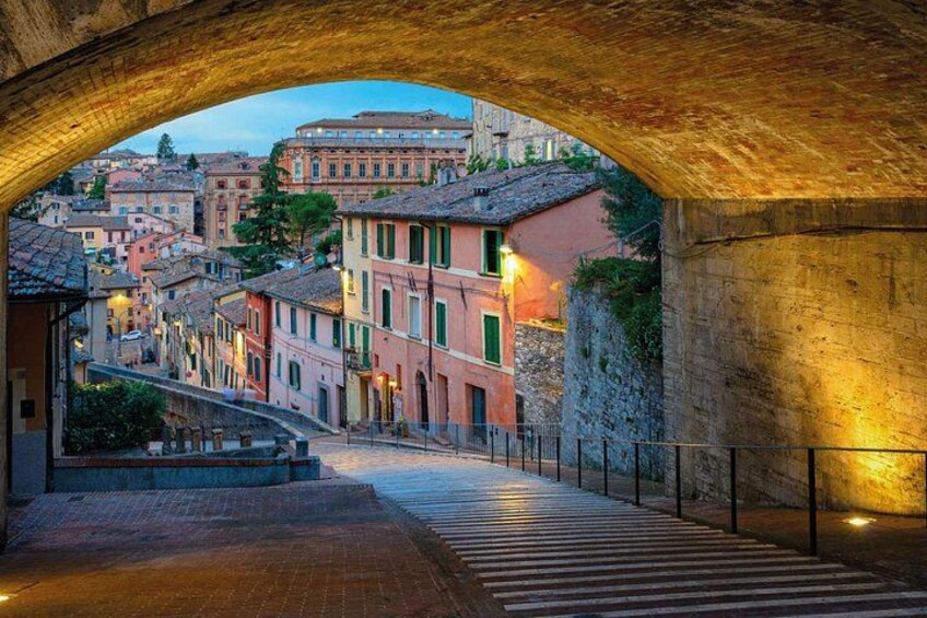 Un pont en pierre, dont l’arche s’étend au-dessus d’un chemin pavé menant à une place de ville aux couleurs vives. 4