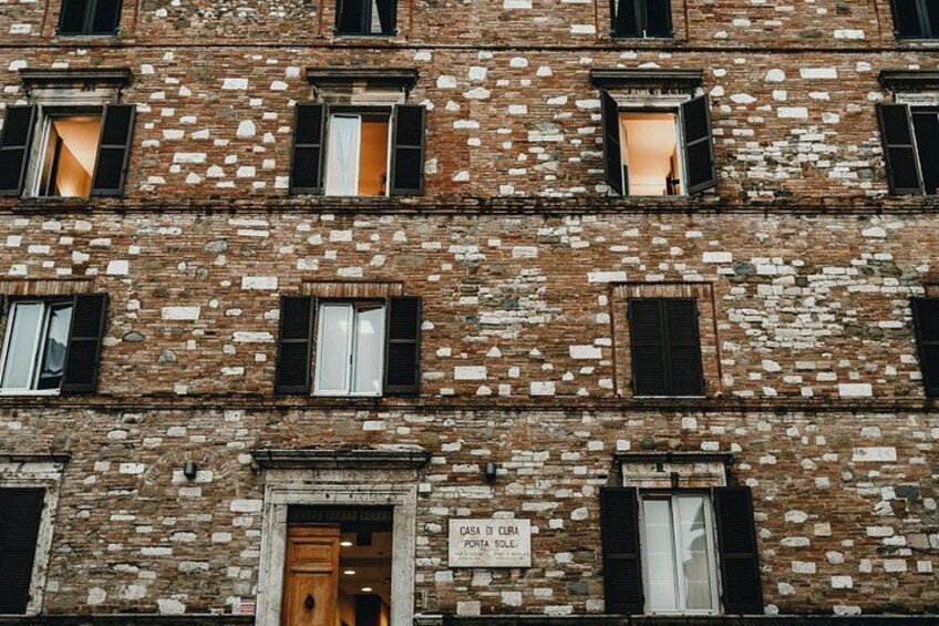 Un immeuble en briques à plusieurs étages, doté de nombreuses fenêtres, dont certaines sont pourvues de volets, et d’une enseigne sur laquelle on peut lire : « LA SALA DI L’URLA ». 5