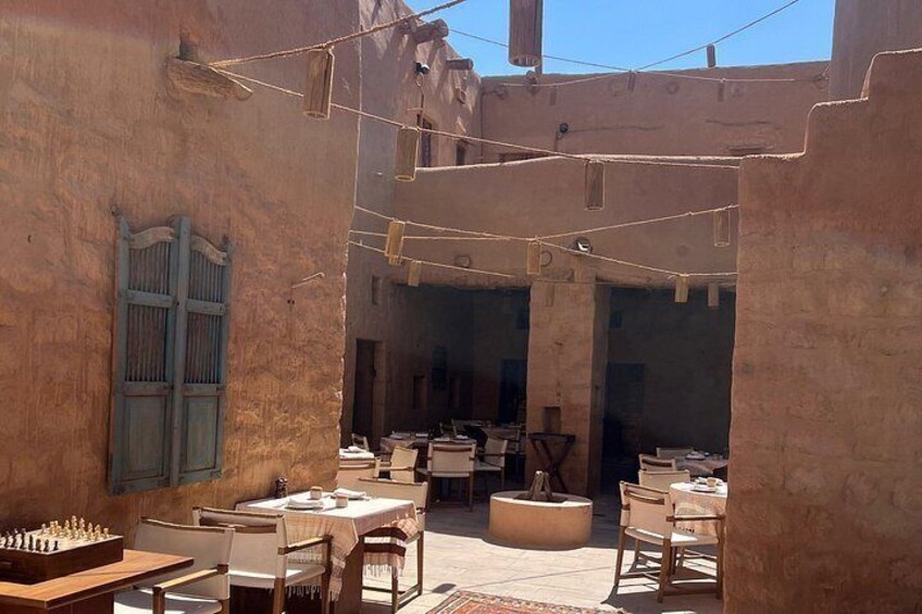 An outdoor dining area with tables and chairs, a chessboard, and a rustic building with a blue shutter. 2