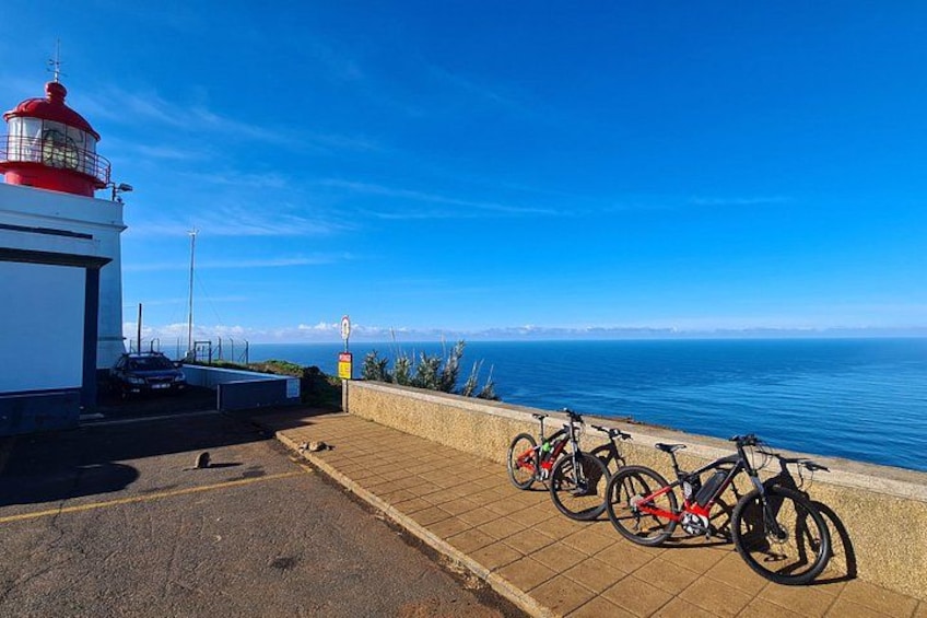 A lighthouse, a paved walkway, and bicycles parked by the seaside. 3