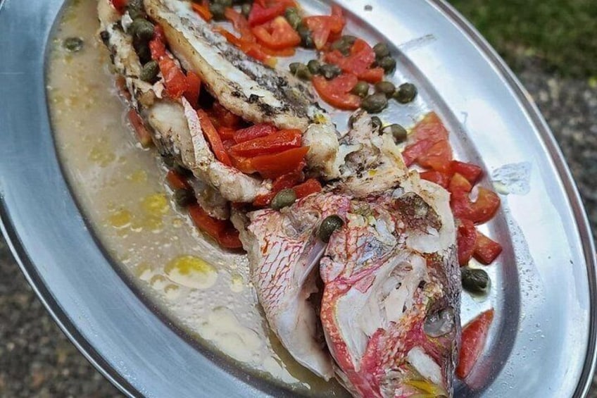 Un plato de pescado con pimientos rojos y alcaparras sobre una bandeja de metal. 3