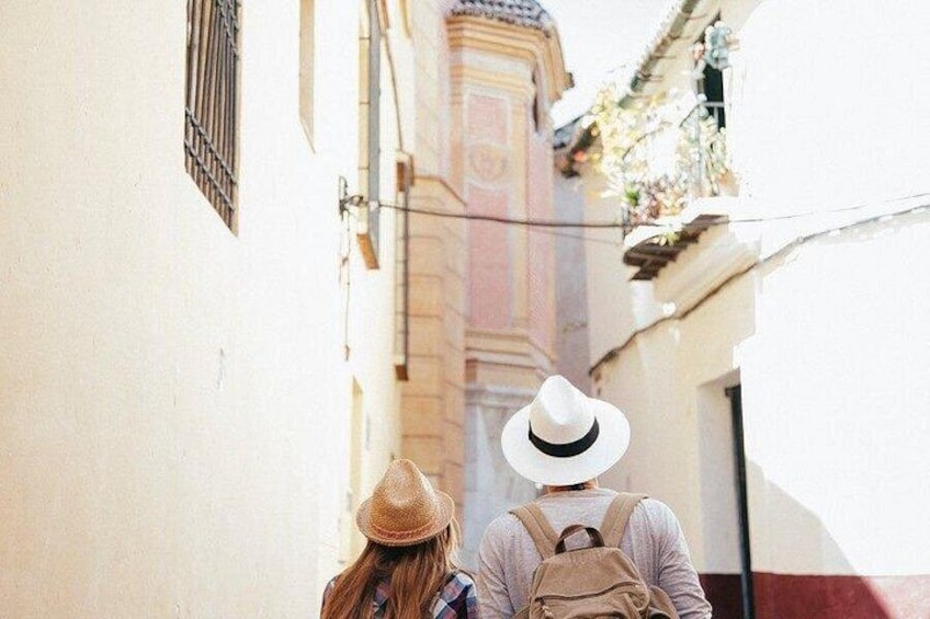 Una calle estrecha flanqueada por edificios, una persona con sombrero y una mochila, y otra persona con una mochila. 2