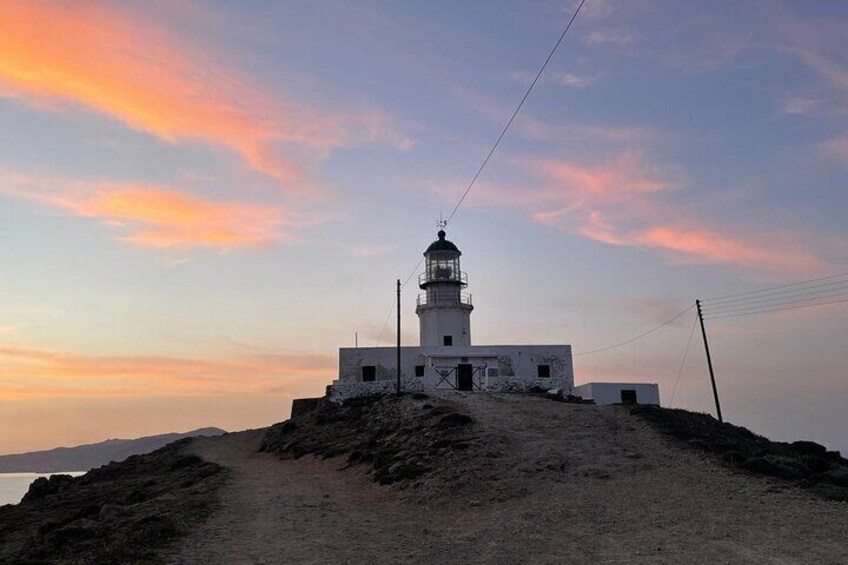 A lighthouse on a rocky outcrop with a dirt path leading to it, under a sunset sky. 1