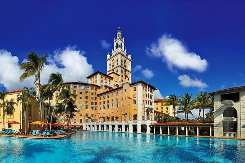 Een hotel met een groot zwembad, palmbomen en een helderblauwe lucht. 5