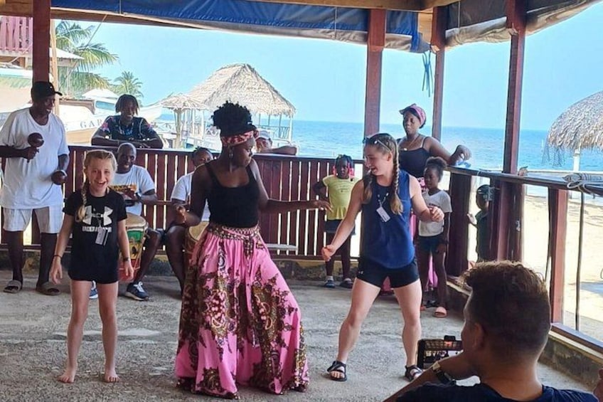 A group of people dancing on a beachside stage with a view of the ocean. 1