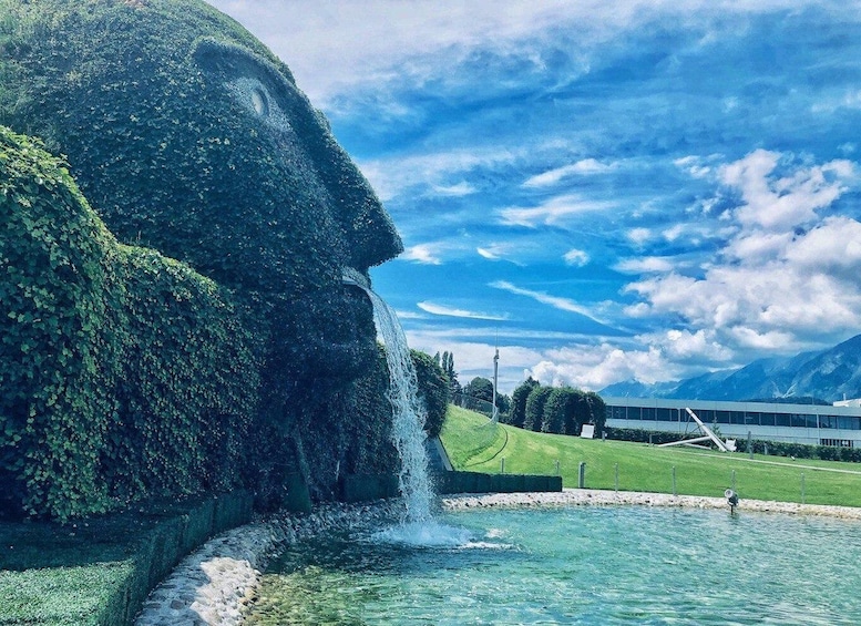 A large rock formation with a waterfall, a clear blue sky, and mountains in the background. 1