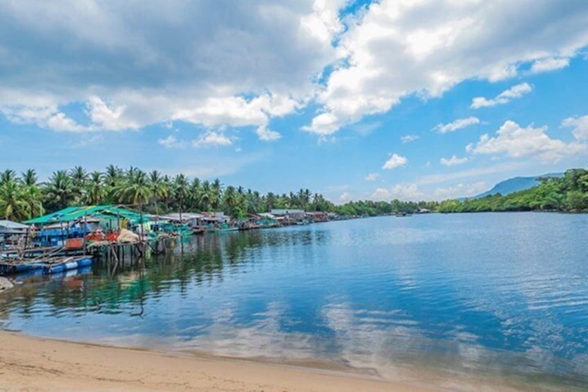 A calm lake with boats, a sandy beach, and palm trees under a partly cloudy sky. 2
