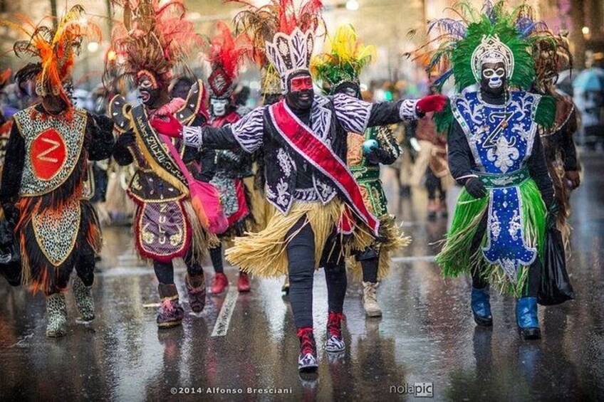Een groep mensen in kleurrijke kostuums met uitgebreide hoofdtoppers en maskers, lopend over een natte straat. 5