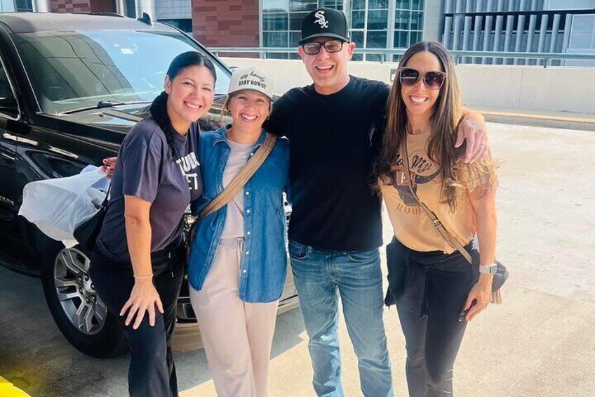 Four people standing in front of a black car in a parking lot. 5