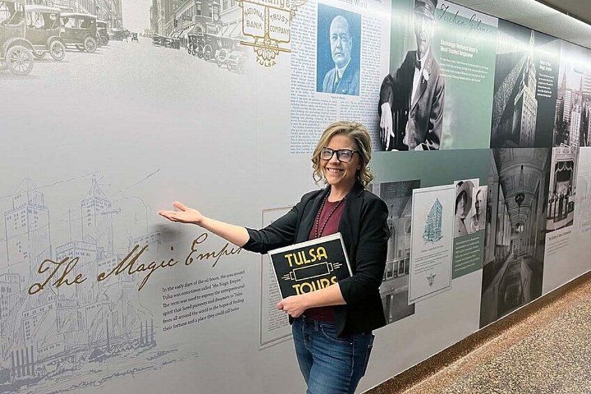 A person standing in front of a wall with historical photos and text, holding a sign that says 'Tulsa TOURS.' 5