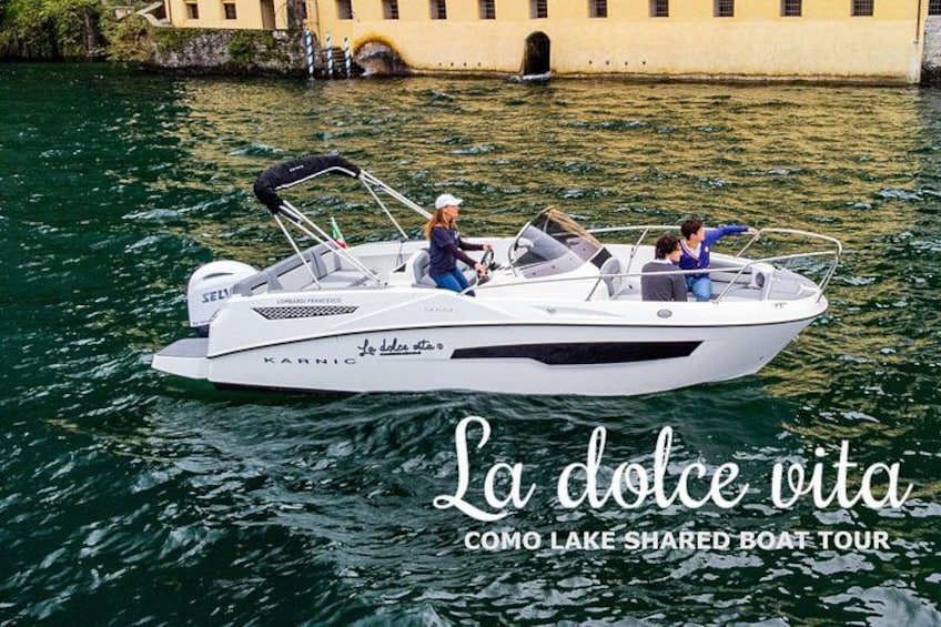 A white motorboat on water with two people, a building in the background, and text overlay. 1