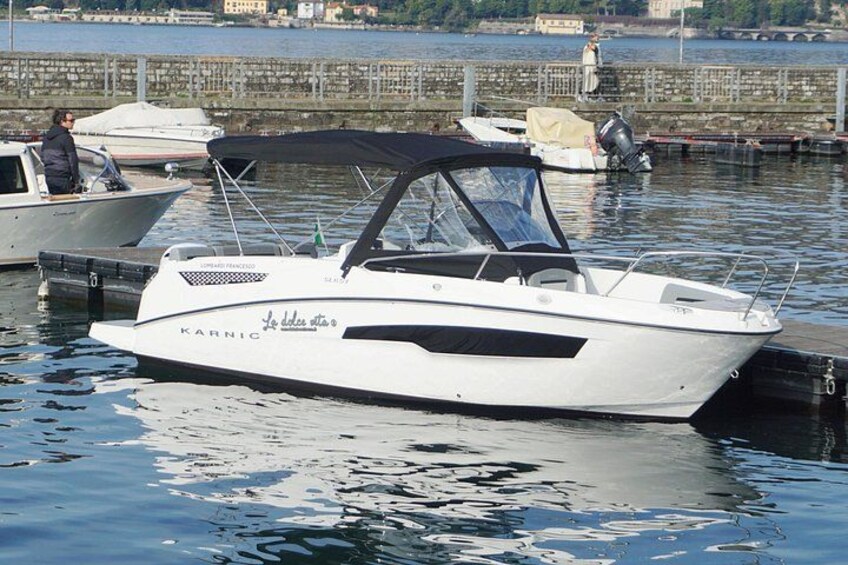 Un barco a motor blanco llamado 'Karnic' amarrado en un puerto deportivo, con aguas tranquilas y un muro de piedra al fondo. 1