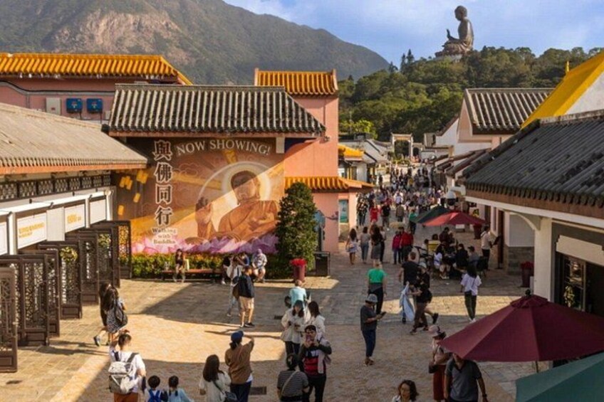 A traditional street with people walking, a large Buddha statue in the background, and a sign with Chinese characters. 2