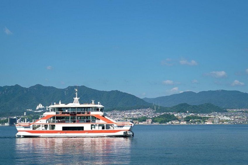 A large ferry boat on calm waters with a cityscape and mountains in the background. 3