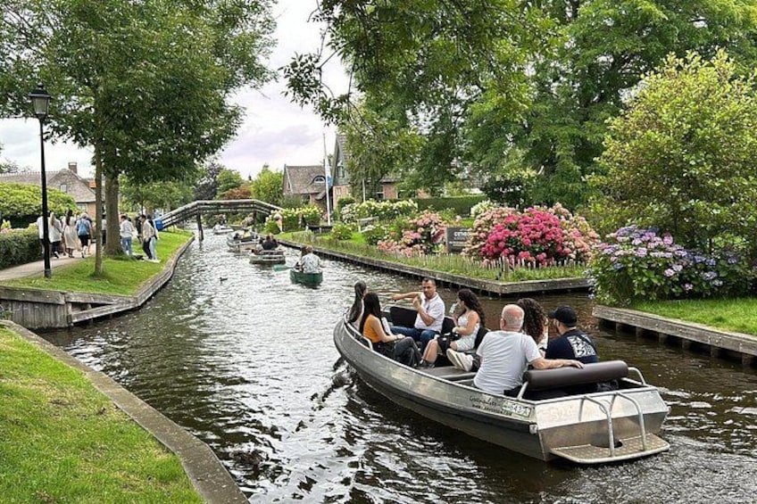A canal with boats, people walking on the banks, and flower gardens. 1