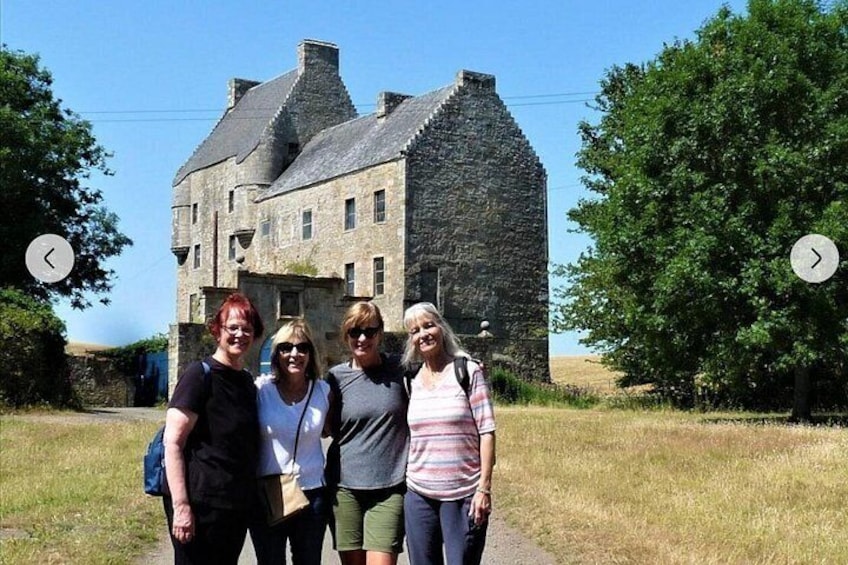 A group of people standing in front of a stone building with a grassy field and trees in the background. 5