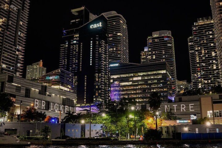 Un horizonte urbano nocturno con edificios iluminados, incluyendo un cartel prominente que dice 'este' en un rascacielos. 3
