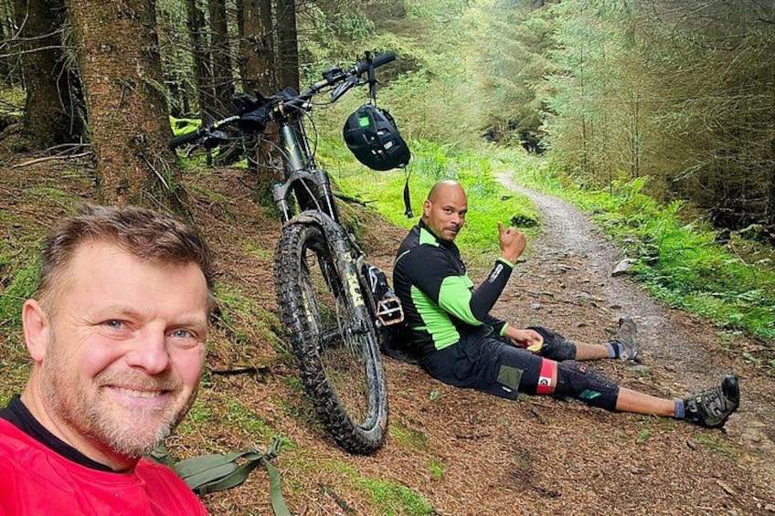 A person sitting on a forest trail with a mountain bike and helmet beside them. 4