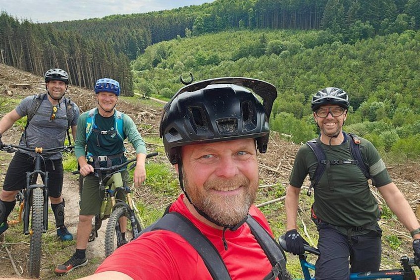 A group of mountain bikers on a trail with forested hills in the background. 1