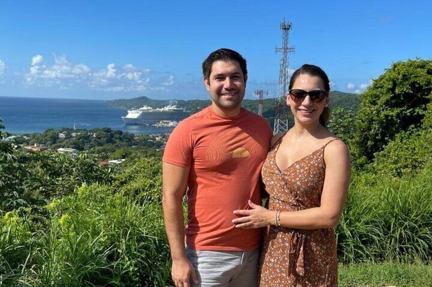A couple standing on a grassy hill with a view of the ocean and a power line tower in the background. 5