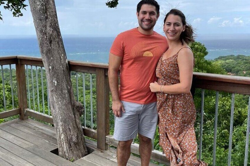 A couple standing on a wooden deck with a view of the ocean and greenery. 4