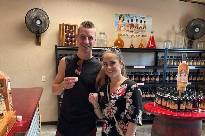 Two people in a distillery with shelves of bottles and a sign that says "Meet the locals!" 3