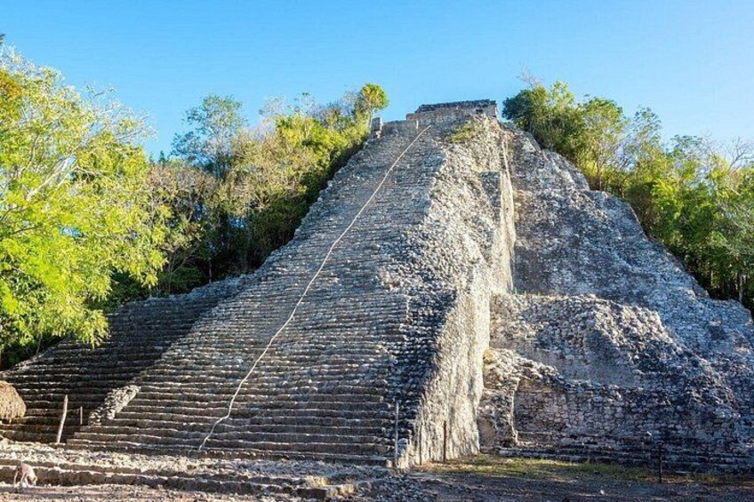 Eine große Pyramide mit einer Treppe, die zum Gipfel führt, umgeben von Bäumen. 1