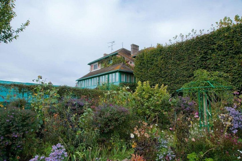 A house with a green roof, a garden with various flowers, and a hedge. 2