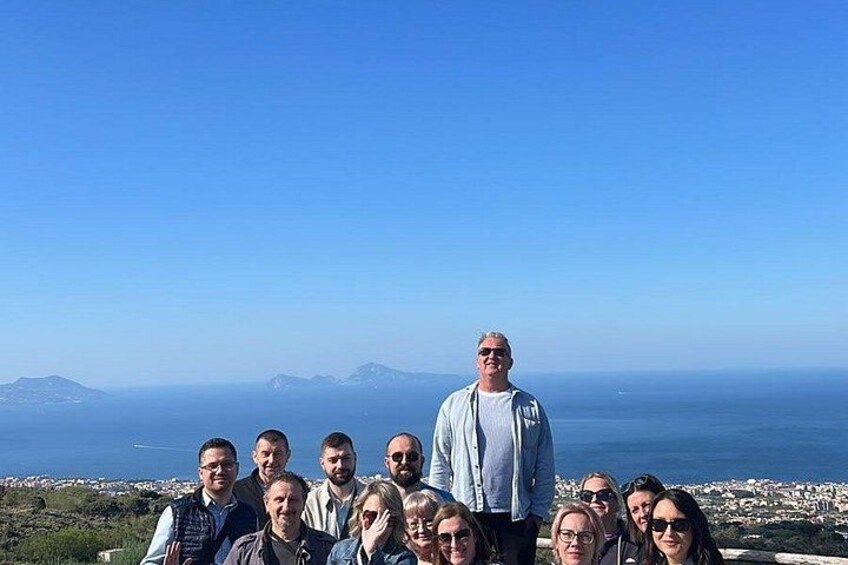 Eine Gruppe von Menschen steht auf einem Hügel und blickt auf eine Küstenstadt mit blauem Himmel. 4