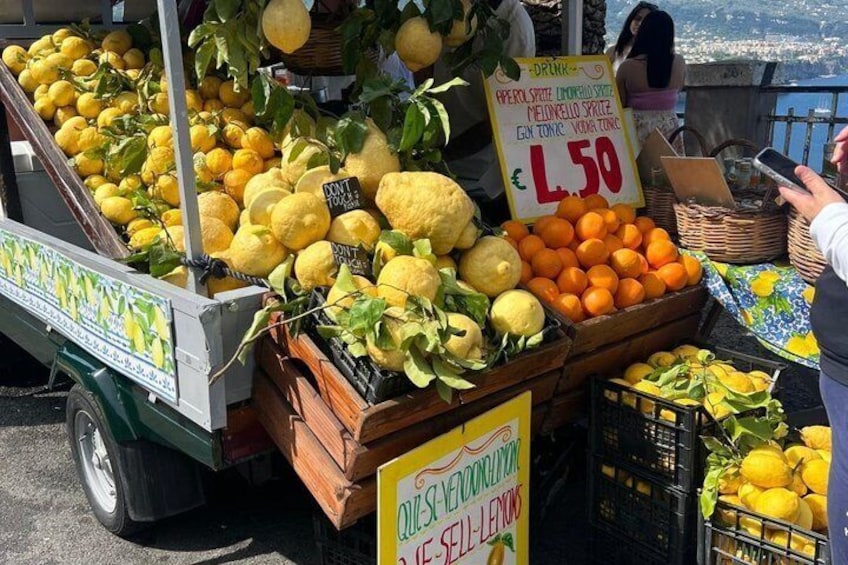 A fruit stand with lemons and oranges, a sign indicating a price of €1.50, and a person using a smartphone. 3