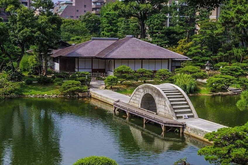 Een traditioneel Japans gebouw met pannendak, een stenen brug met gebogen boog en een vijver. 2