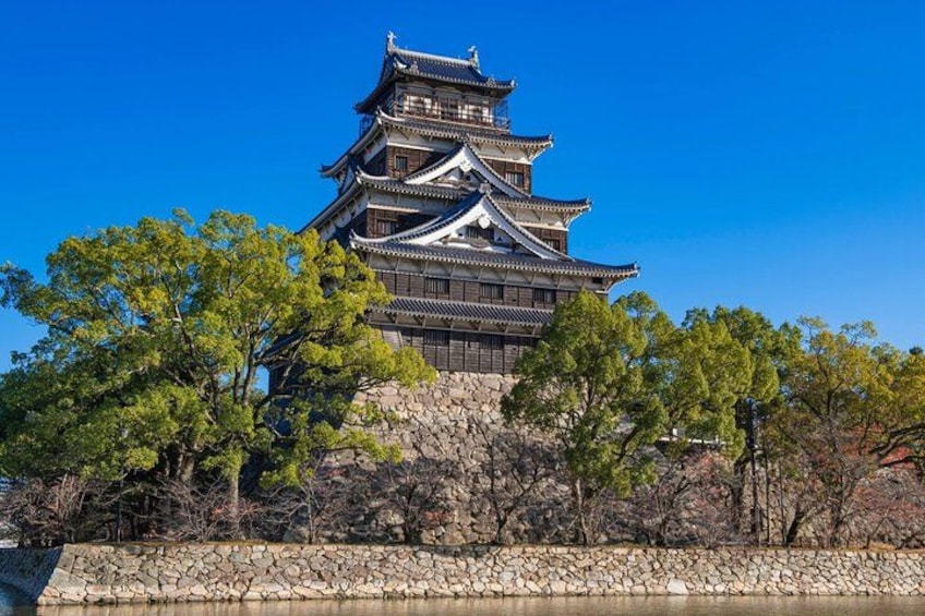 Een traditioneel Japans kasteel met meerdere verdiepingen, omgeven door bomen en een stenen muur. 3