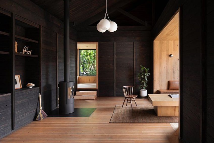 A modern interior with wooden floors, a black stove, a wooden bench, and a hanging light fixture. 2