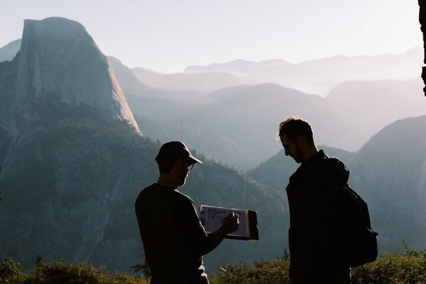 Two people standing on a mountain with a large rock formation in the background. 1