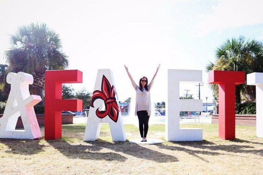 A person standing between large letters spelling 'FAET' with a red flower design on the 'A'. 2