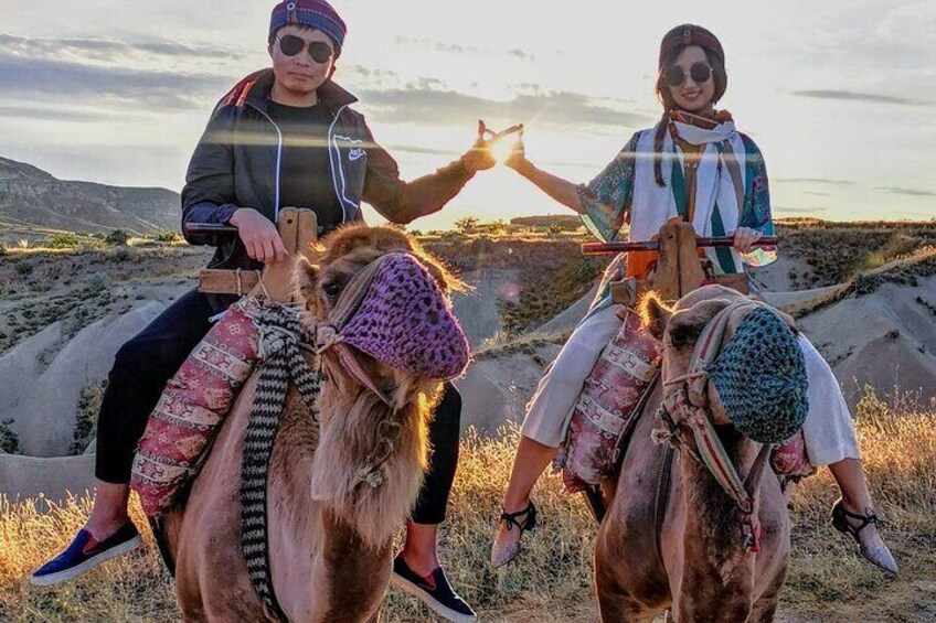 Dos personas montando camellos en un paisaje desértico con el atardecer de fondo. 4