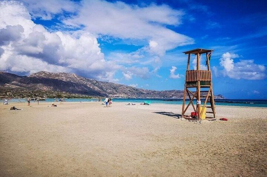 Ein Strand mit einem Rettungsturm, blauem Himmel und Bergen im Hintergrund. 1