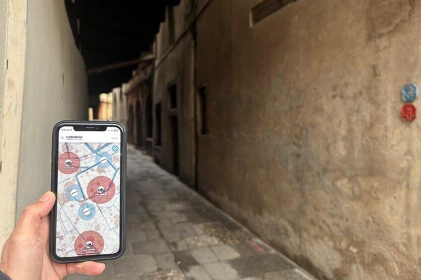 Un teléfono inteligente mostrando un mapa con ubicaciones marcadas, sostenido por una persona en un callejón con edificios. 2
