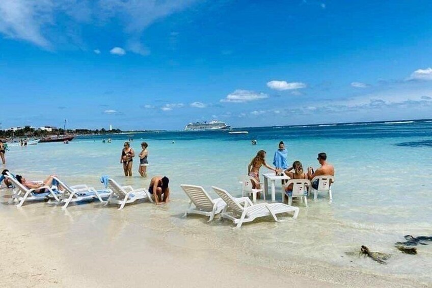 Una playa con gente tomando el sol y nadando, un cielo azul despejado y un barco a lo lejos. 2