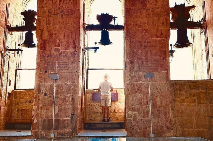 A person standing in front of a large bell tower with stone columns and a window. 2