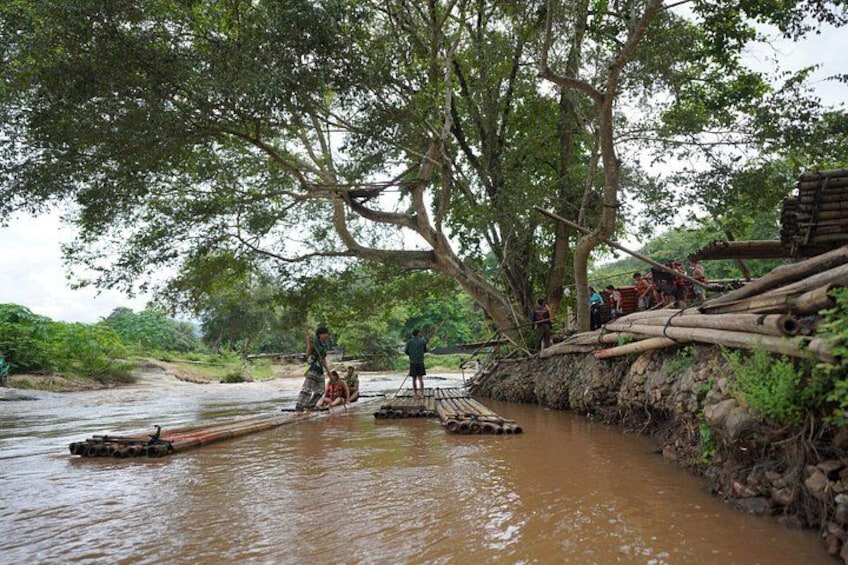 A river with people crossing on a makeshift bridge made of logs and a boat on the water. 4