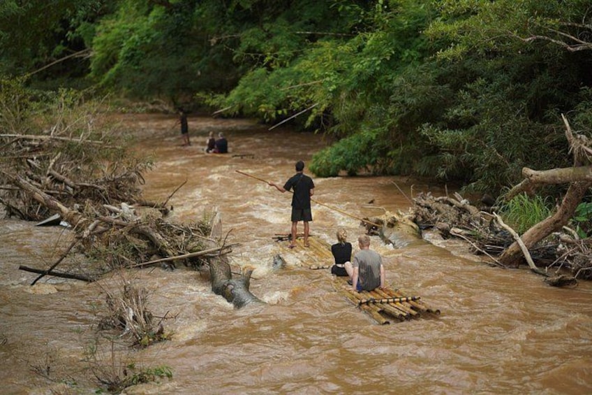 A river with people crossing on a makeshift raft, surrounded by dense greenery. 3