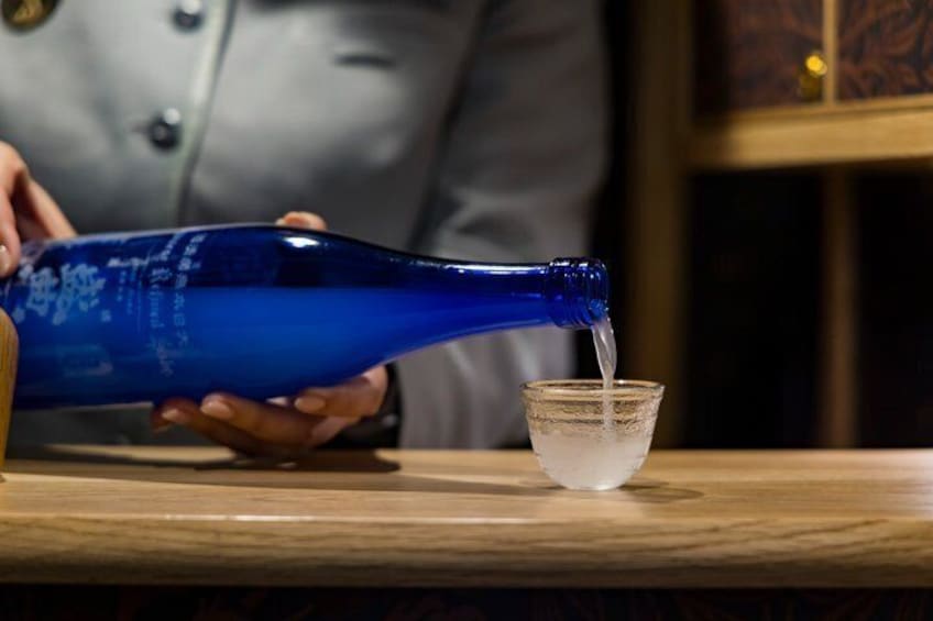 Una persona vertiendo un líquido transparente desde una botella azul en un vaso. 3